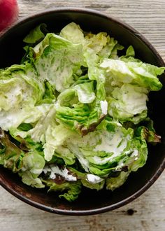 lettuce in a brown bowl with white dressing on the top and green leaves