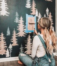 a woman sitting on the floor in front of a wall with trees painted on it