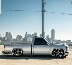 a silver truck parked on top of a parking lot next to a tall city skyline