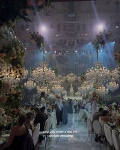 people sitting at tables in front of chandeliers with flowers and candles on them