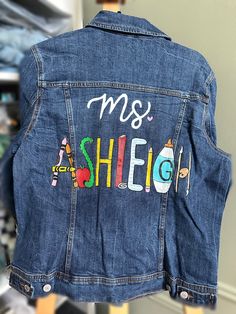 the back of a jean jacket that says, mrs sheig on it and has school supplies painted on it