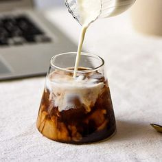 a person pouring milk into a glass on a table with a laptop in the background