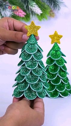 someone is holding two small christmas trees made out of paper and glittery glues