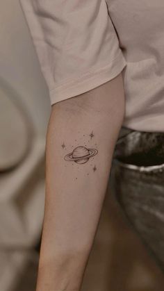 a small saturn tattoo on the left inner arm, with stars in the sky above it