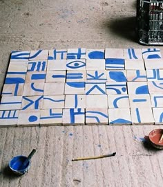 some blue and white tiles sitting on the ground next to bowls with paintbrushes