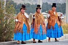 three women dressed in brown and blue are standing on the side of the road with their hands up