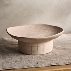 a white bowl sitting on top of a wooden table next to a gray cloth covered napkin