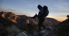 a man hiking up the side of a mountain in the evening with his backpack on