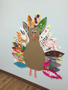 a turkey made out of paper and colored feathers on a wall with wood flooring