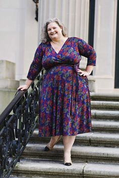 a woman in a purple dress standing on some steps with her hands on her hips