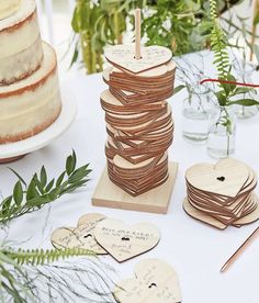 a table topped with lots of wooden heart shaped coasters next to a cake covered in greenery