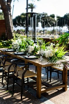 an outdoor dining table set with flowers and greenery