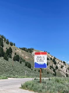 a sign that is on the side of a road in front of a hill and trees