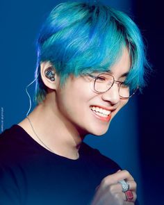 a person with blue hair and glasses smiling