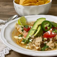 a white plate topped with chicken and veggies next to a bowl of tortilla chips