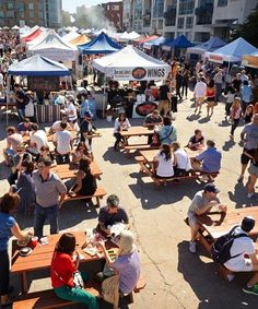 a crowd of people sitting at picnic tables in front of tents with food on them