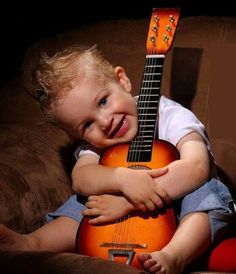 a young boy is holding an orange guitar