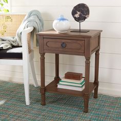 a wooden table with a lamp and books on it next to a white chair in a room