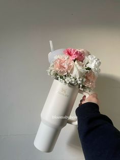 a person is holding a flower arrangement in front of a white cup with a straw