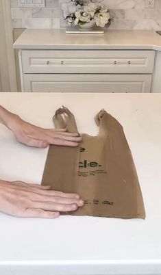 two hands holding a brown paper bag on top of a white counter in a kitchen