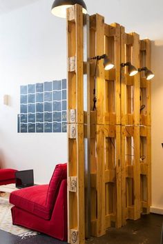 a living room with a red couch and wooden partition in the wall between two chairs