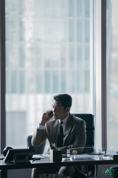 a man sitting at a desk in an office talking on a cell phone and holding a pen to his ear