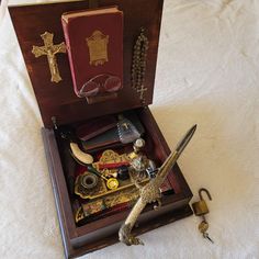 an open wooden box filled with assorted items on top of a white tablecloth