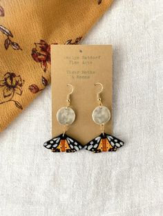 Title: Tiger Moths & Moons Looking for a unique handmade addition to your jewelry box? This pair of lovingly hand-painted wooden earrings will add artistic flair to your wardrobe or a personal touch to your gift to a loved one.  These original handcrafted earrings are hand painted on balsa wood with sterling silver hooks for sensitive ears (the gold hooks are gold plated sterling silver). Each pair of earrings in my shop is carved and painted by hand, and the item you receive is the exact one seen in the photos. The earrings are lightweight and hypoallergenic. This gift can be personalized with a special note and sent directly to friend or loved one. Please add the note during checkout using the box Etsy provides for "Notes to Seller." Looking for a different design? Check out my shop to f Artsy Earrings, Wooden Butterfly, Body Accessories, Gold Hooks, Balsa Wood, Polymer Clay Jewelry Diy, Painted Jewelry, Clay Earring, Earring Ideas