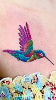 a colorful hummingbird tattoo on the back of a woman's shoulder