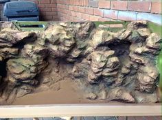 a close up of a fake rock formation on a bench near a brick wall and garbage can