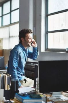 a man talking on his cell phone while sitting at a desk in front of a computer