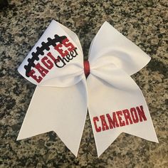 Cheer bow with football laces on upper loop. Any text can be done upper loop and tail. Bow comes with cheer unless otherwise noted.  Great sideline and game day bow. Custom bows for your squad. 3" x 28" grosgrain ribbon with glitter heat transfer vinyl and ponytail elastic attached. Bow is approx 7" wide by 7"tall.  Message me for any ideas or how you would like to customize. Bulk orders welcome for teams. Football Cheer Bows, Cheer Bow Ideas, Holiday Cheer Bows, Cheer Fundraiser, Girls Activities, Bow Business, Cute Cheer Bows, Cheer Season, Sideline Cheer