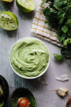 an avocado dip in a white bowl surrounded by limes and cilantro