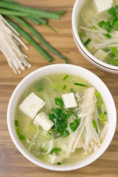 two bowls of soup with tofu, green onions and scallions on a wooden table