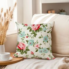 a flowered pillow sitting on top of a couch next to a cup