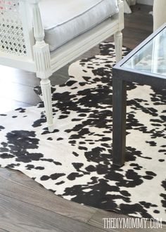 a cow print rug with a glass table in the middle and a white chair at the end