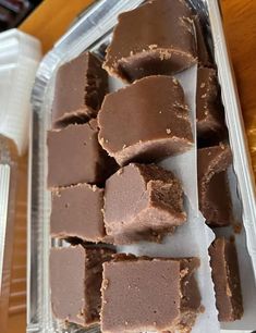 several pieces of chocolate fudge sitting on top of a plastic container next to a cup