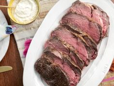 a large piece of meat sitting on top of a white plate next to a knife and fork