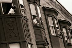 black and white photograph of people looking out the windows on an old brick apartment building