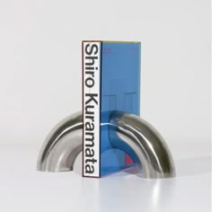 a book sitting on top of a metal object in front of a white wall with a blue box