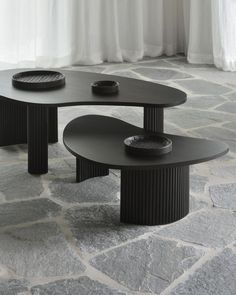 two black tables sitting next to each other on top of a stone floor in front of a window