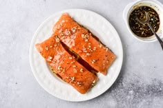 two pieces of salmon on a white plate next to a small bowl of seasoning