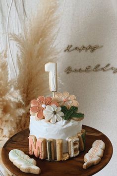 a cake decorated with flowers and the number one on top is sitting on a wooden plate