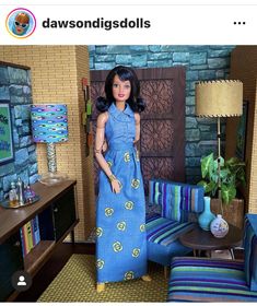 a doll in a blue dress standing next to a couch and table with a lamp on it