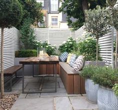 a wooden bench sitting under a tree next to a white fence and some plants on top of it