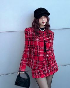 a woman in a red coat and hat holding a black purse standing next to a wall