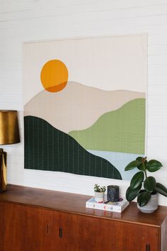 a wall hanging above a dresser with a potted plant next to it and a painting on the wall