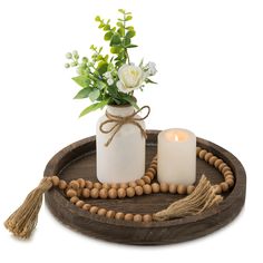 two candles are sitting on a wooden tray with beads and flowers in the vases