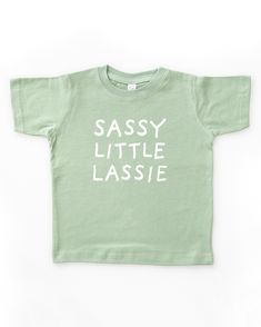 Light sage green short sleeve toddler crew neck tee with white SASSY LITTLE LASSIE print in a handwritten font Toddler Tshirt Ideas, Neutral Bodysuit, Toddler Graphic Tee, Funny Toddler Shirt, Shirt Quotes, St Patricks Day Shirt, Toddler Humor, Text Tee, Toddler Mom