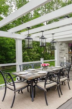 an outdoor dining table and chairs on a covered deck with lights hanging from the ceiling